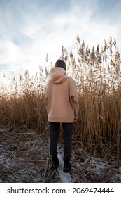 Vertical Banner With A Model In Oversized Beige Hoodie In Reeds.back View.fashion And Wear Concept.warm Oversize Wear At Woman.space For Text And Logo.mock Up For Print.female Standing In Reeds