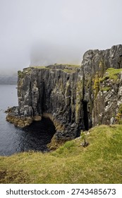 Vertical basalt rock formations drop into the dark Atlantic Ocean under a heavy blanket of mountain fog.