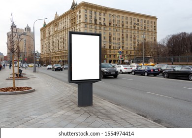 Vertical Billboard In The City By The Road Against The Background Of The Yellow Building Of The Old Style.