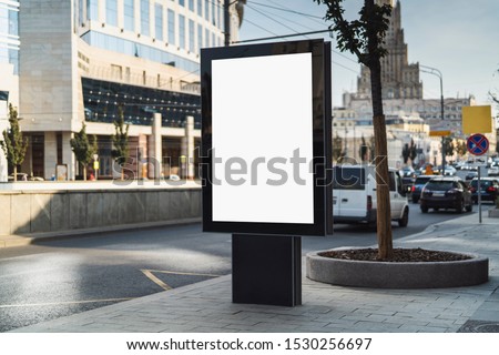 Vertical billboard for dispaying commercials in street. Cars and public transport passing by. Urban architecture of big city in background. Sidewalk for pedestrians, great place for promotional ads.