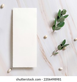 Vertical Card On A Marble Table Decorated With Eucalyptus Branches And White Stones Top View, Wedding Mockup. Romantic Flat Lay With Blank Menu Card. Minimal Composition. Close To Nature 