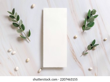 Vertical Card On A Marble Table Decorated With Eucalyptus Branches And White Stones Top View, Wedding Mockup. Romantic Flat Lay With Blank Menu Card. Minimal Composition. Close To Nature 