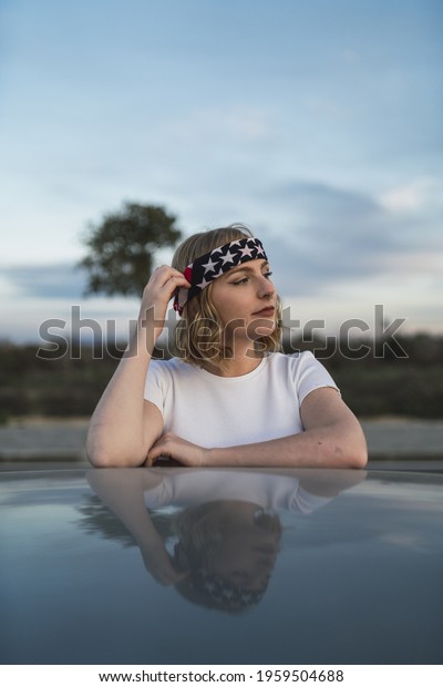 A vertical of a Caucasian\
female wearing an American flag bandana and resting on the side of\
a road
