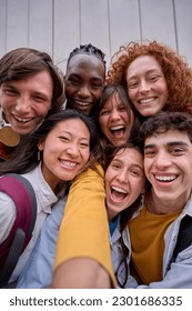 Vertical cell phone selfie of excited multiracial group of erasmus college students together outside. Cheerful smiling young friends pose laughing for photo. Happy people on campus.