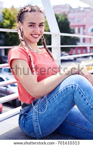 Vertical of charming youth listening to music while sitting under handrail
