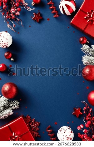 Vertical Christmas flat lay composition with red gift, frosted pine branches, and ornaments on dark blue background. Elegant seasonal design.