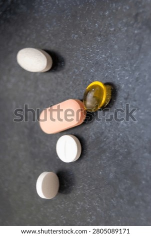 A vertical close up framing of multiple clinical medication pills, health tablets, and a golden oil supplement capsule on a grey stone texture.