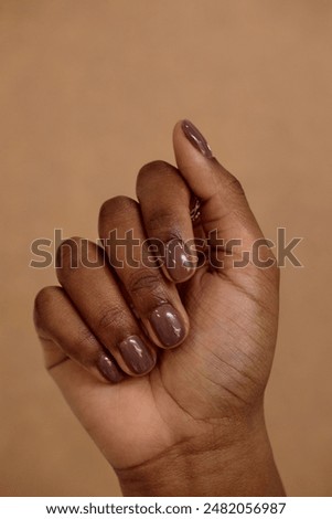 Vertical close up on dark brown manicure of African American girl on beige background. Nail minimalistic nude design ideas