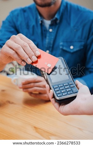 Vertical close up portrait of a male customer paying a bill with a contactless credit card in a restaurant. Man hand holding a creditcard and giving a payment transaction to the cashier. High quality