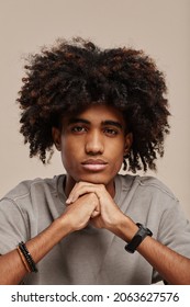 Vertical close up portrait of young African-American man with natural curly hair looking at camera in studio against beige background