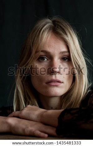  vertical close up studio  headshot of blond nordic woman with brown eyes with melancholic expression on sad face with black background and natural light