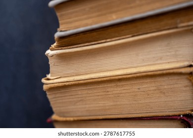 Vertical close up of a tall stack of old antique and secondhand books with weathered multi colored covers and aged yellowed pages, representing literature, history, and education.