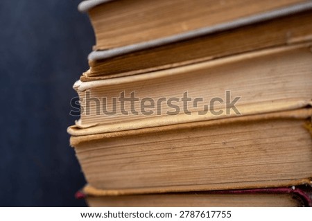 Vertical close up of a tall stack of old antique and secondhand books with weathered multi colored covers and aged yellowed pages, representing literature, history, and education.
