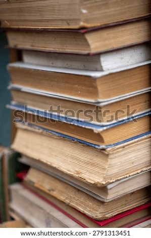 Vertical close up of a tall stack of old antique and secondhand books with weathered multi colored covers and aged yellowed pages, representing literature, history, and education.