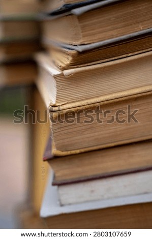 Vertical close up of a tall stack of old antique and secondhand books with weathered multi colored covers and aged yellowed pages, representing literature, history, and education.