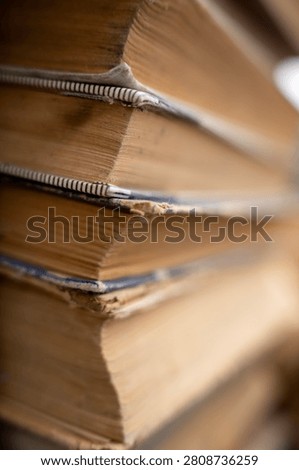 Vertical close up of a tall stack of old antique and secondhand books with weathered multi colored covers and aged yellowed pages, representing literature, history, and education.