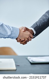 Vertical Close Up Of Two Business People Shaking Hands At Meeting Against Simple Blue Background