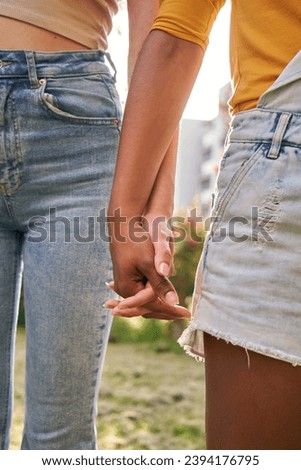 Vertical close up of two multiracial unrecognizable women holding hands outdoor. Young adult girls friends standing together summer outdoors. Concept of friendship and same-sex union.