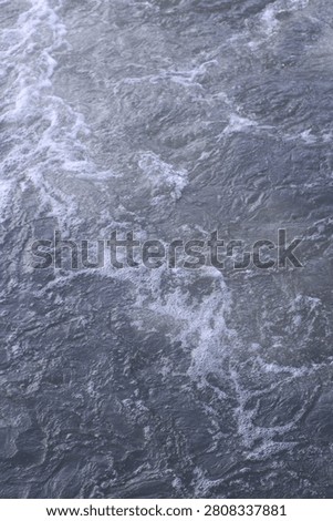 Vertical close-up background texture of fast flowing river water with bubbling white foam