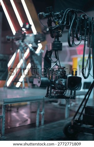 Vertical close-up of a broadcast camera on a remote head system in a television studio with neon lights