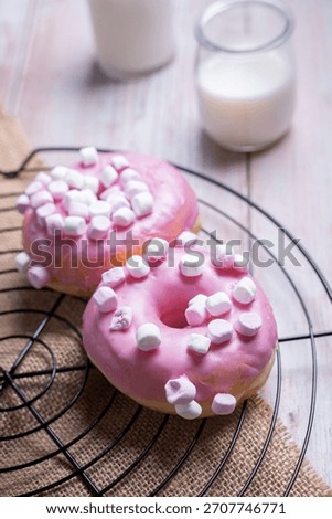 A vertical closeup of donuts with marshmallows next to glasses of milk