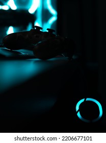 A vertical closeup of a game controller in the darkness with glowing blue neon lights 