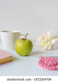 Vertical Closeup Of Green Apple On Table With Self Care Items In Background Including Crochet, Flower, Cup, Journal (selective Focus)