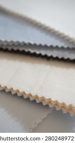 Vertical close-up of layered fabric samples in blue, grey and beige. Zigzag cut edges show textile texture. Material selection for interior design or clothing.
