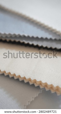 Vertical close-up of layered fabric samples in blue, grey and beige. Zigzag cut edges show textile texture. Material selection for interior design or clothing.