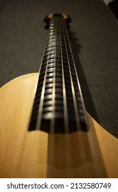 A vertical closeup of the mandolin neck and strings on the gray textured surface 