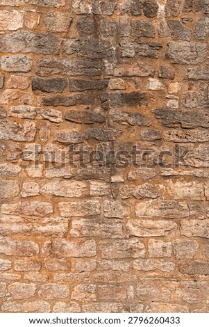 Vertical close-up of an old stone wall texture with irregular masonry, warm natural colors, rough surface, and historic architectural detail