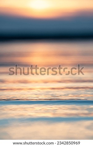 A vertical closeup shot of the surface of the water reflecting the colors of sunset