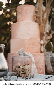 A Vertical Closeup Of A Small Glass Jar Of Cookies With A Big Cake In The Background 