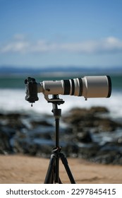 A vertical closeup of surf photography telephoto lens and camera body on tripod. Jeffreys Bay, Africa.