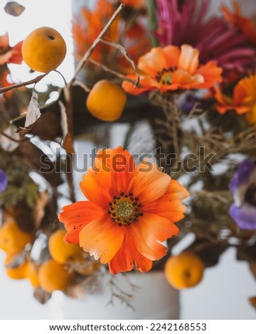 A vertical close-up view of artificial orange flowers and apples in a pot