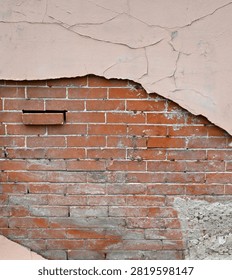 A vertical close-up view of a decaying multi-layer wall surface with tan painted concrete and an inner red brick layer with mortar. The tan painted concrete is scratched, cracked, and pulling away from the inner layers. The red brick layer is weatherworn with a misplaced brick sticking out, cracked and uneven mortar wearing away in places, and a large wall patch is visible in the lower corner.