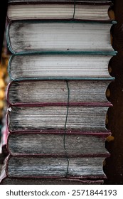 A vertical closeup view of a stack of aged books with faded spines and worn edges