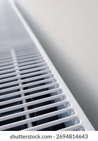 vertical close-up of a white panel heating radiator grill against a minimalist white wall with copy space