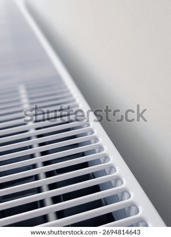 vertical close-up of a white panel heating radiator grill against a minimalist white wall with copy space