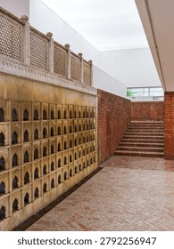 Vertical composition of an architectural space featuring a wall of small arched niches, brick flooring, and stairs leading upwards. The scene conveys history, cultural design, and architectural symmetry.