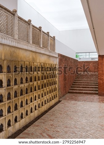 Vertical composition of an architectural space featuring a wall of small arched niches, brick flooring, and stairs leading upwards. The scene conveys history, cultural design, and architectural symmetry.