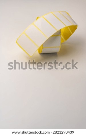 Vertical composition of blank rectangular adhesive labels curling above a white surface.