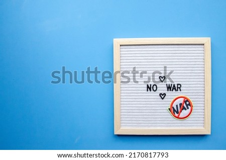 vertical composition with a blue background, a letter board in a wooden frame with the phrase NO WAR and  antiwar patch sticker
