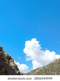 Vertical composition of blue sky above canyon cliffs with bright white cloud and large copy space.