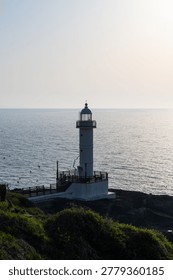 A vertical composition of a classic white lighthouse situated on a green coastal cliff, providing a sense of guidance and tranquility.