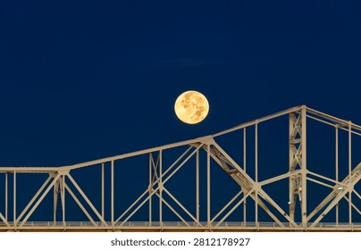 Vertical composition of the full moon dropping behind the steel trusses of the Second Street Bridge in Louisville during a fall 2025 sunrise.