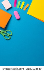 Vertical composition of post its, eraser, crayons and scissors on blue surface with copy space. School equipment, tools and creativity concept.