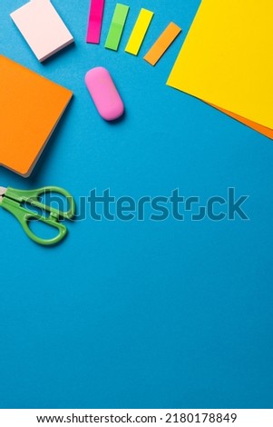 Vertical composition of post its, eraser, crayons and scissors on blue surface with copy space. School equipment, tools and creativity concept.