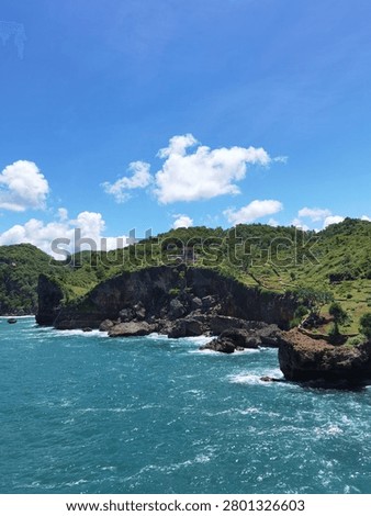 Vertical composition showing a rugged cliff edge jutting into the blue sea at Gunung Kidul.