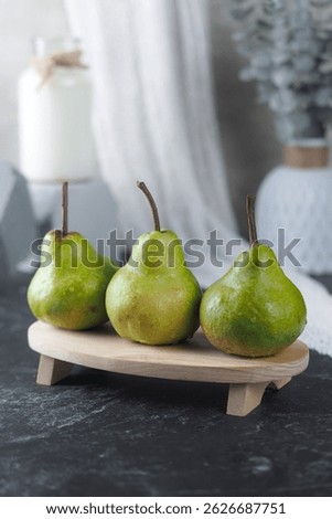 The vertical composition of three fresh green pears with water droplets are neatly arranged on a small wooden tray. 